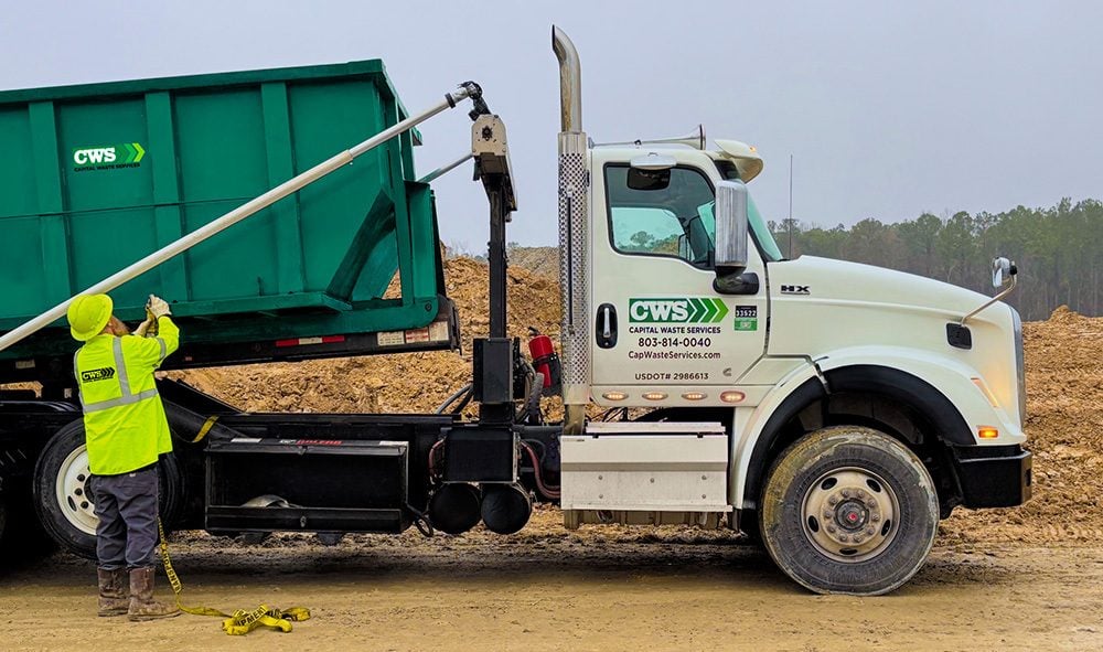CWS employee unloading roll-off dumpster from truck at an industrial site