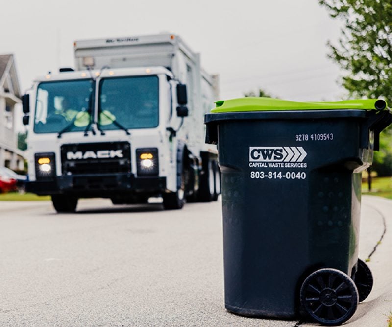 View of recycle bin on a residential street with a collection truck blurred in the background